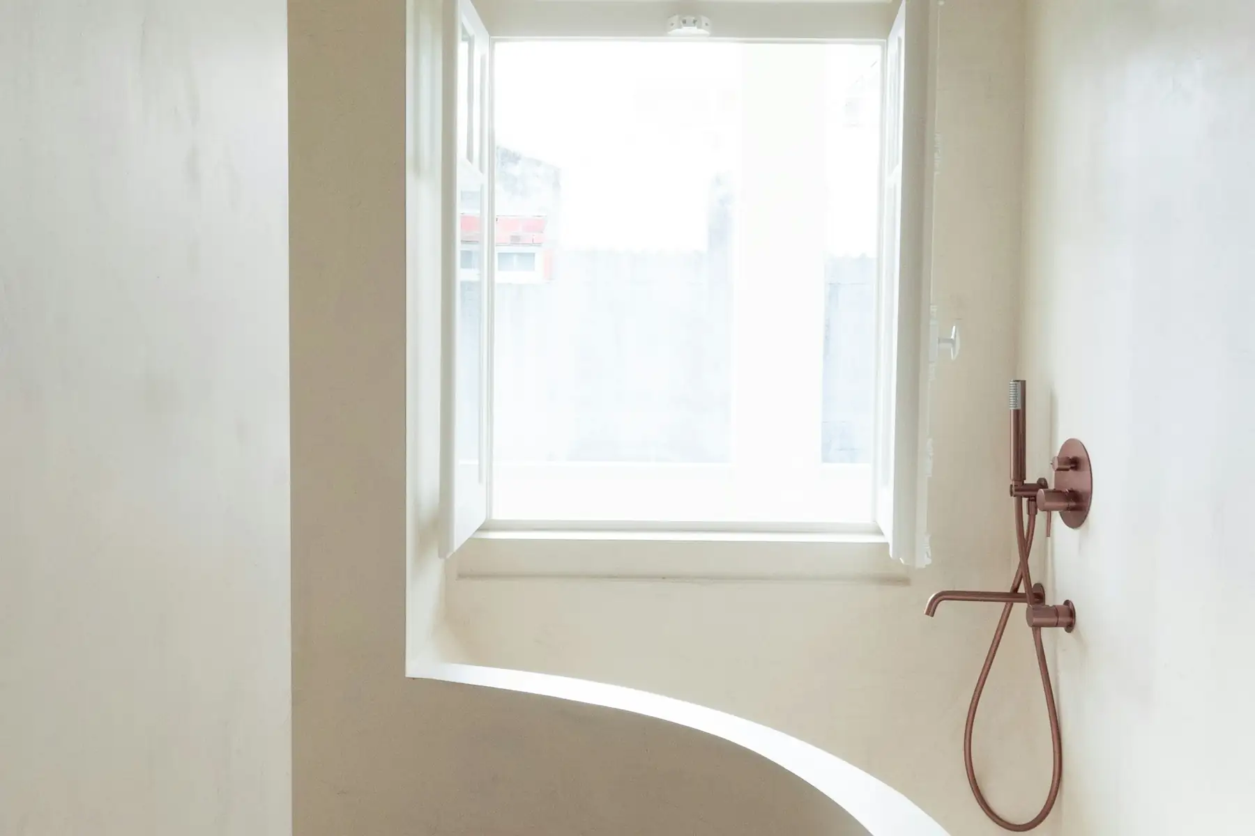 Douche ouverte aux parois claires et lisses, sans joint, sous une fenêtre