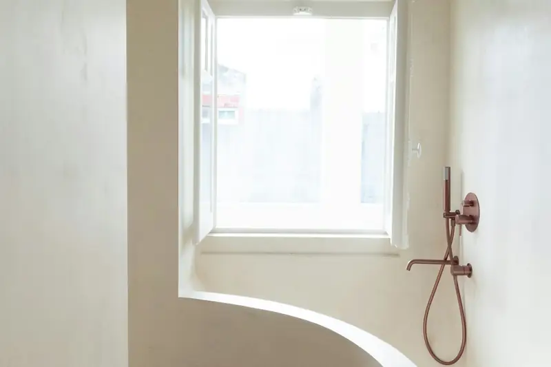 Douche ouverte aux parois claires et lisses, sans joint, sous une fenêtre