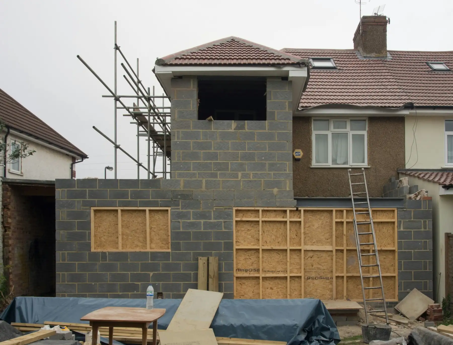 Agrandissement de maison en cours : murs en blocs béton, ouvertures fermées par des panneaux de bois