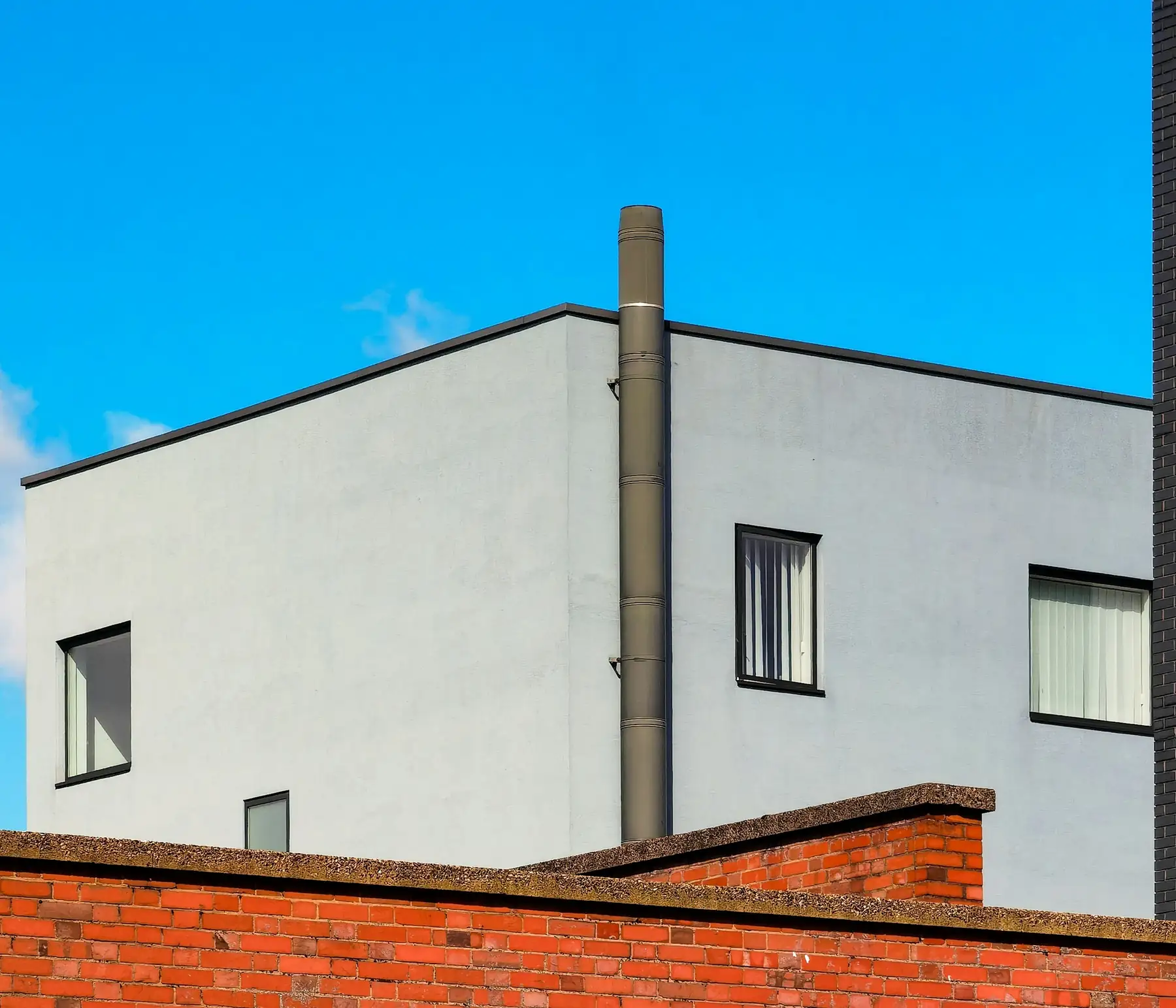 Façade de maison enduite en gris clair, lisse et uniforme, sous un ciel bleu