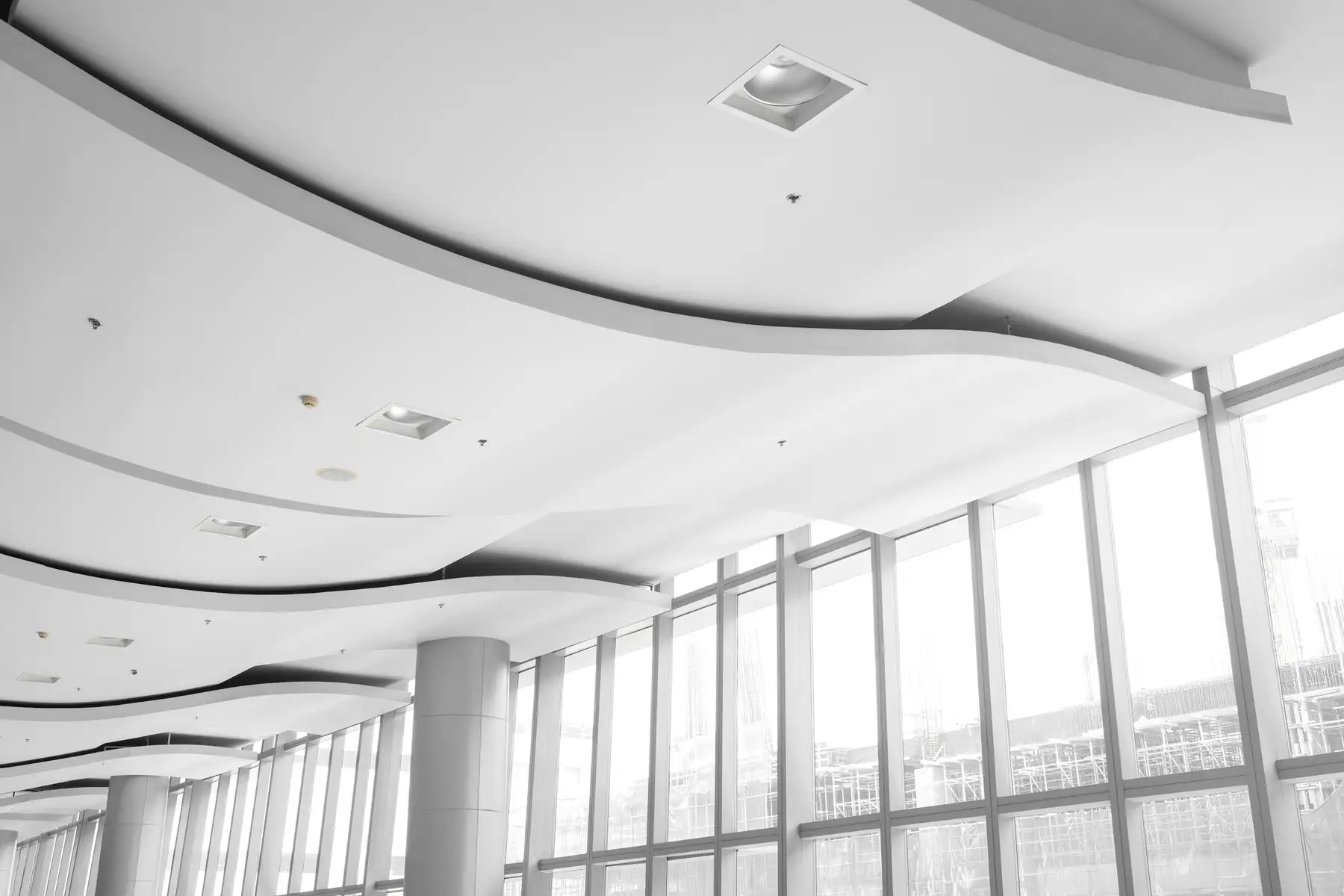 Plafond blanc aux courbes douces avec spots encastrés, grande baie vitrée