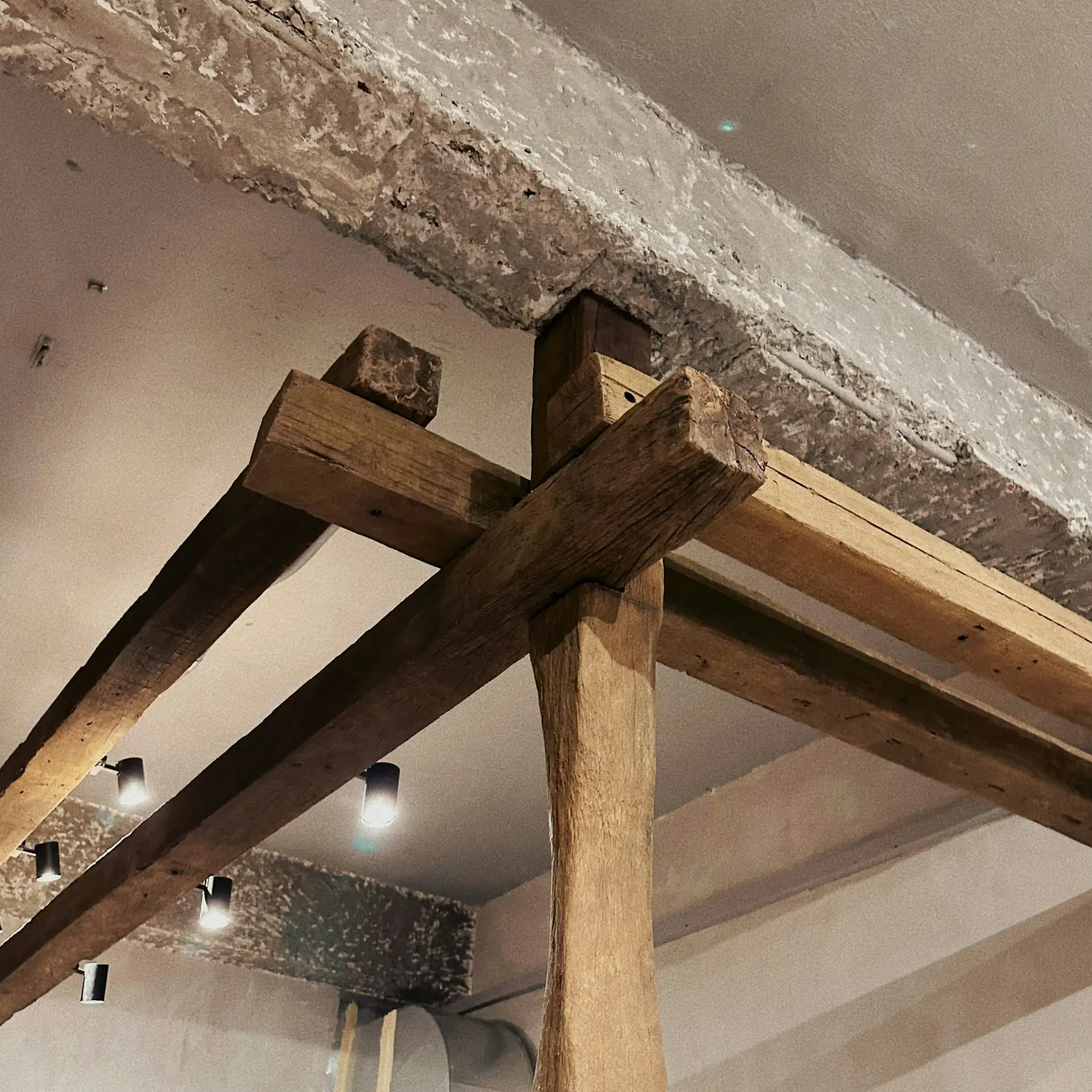 Poutres anciennes en bois brut qui se croisent sous un plafond blanc